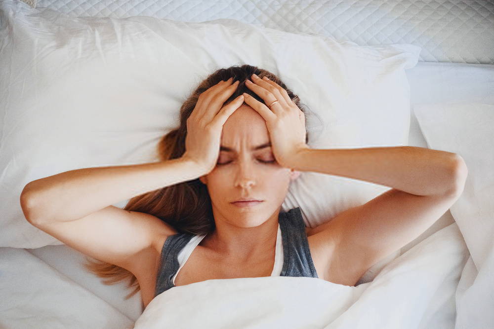 woman in bed with headache as she holds her head