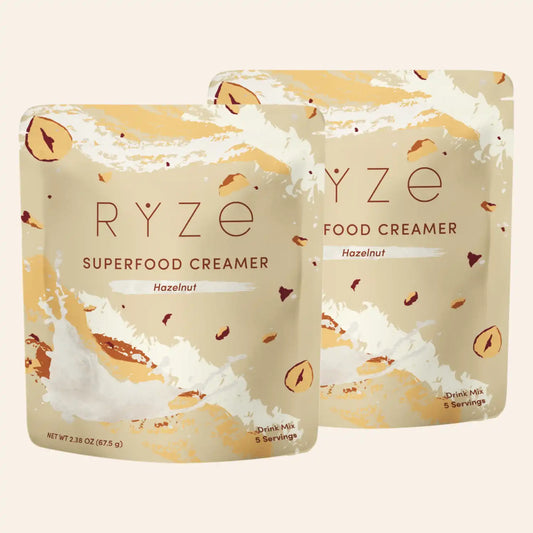 Two pouches of RYZE Food Creamer Superfood Creamer Hazelnut flavor, displayed against a solid light beige background.
