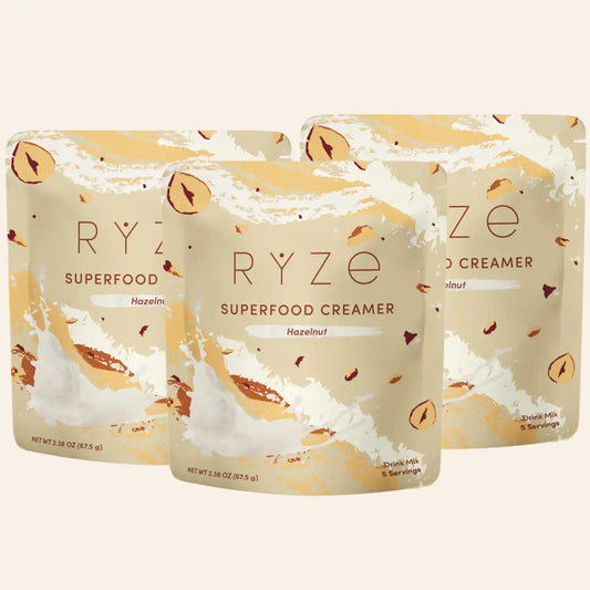 Three stand-up pouches of RYZE Superfood Creamer in Hazelnut flavor, arranged in a fan-like composition on a light beige background.