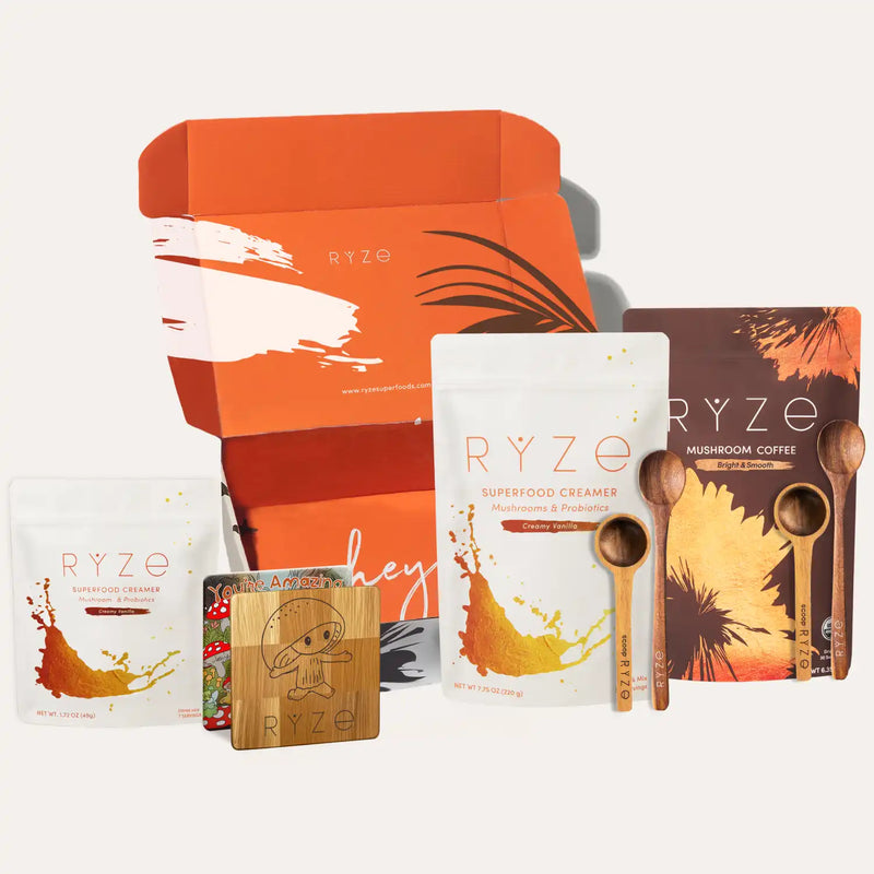 Collection of RYZE products including a box, creamer packets, and wooden spoons on a white background.