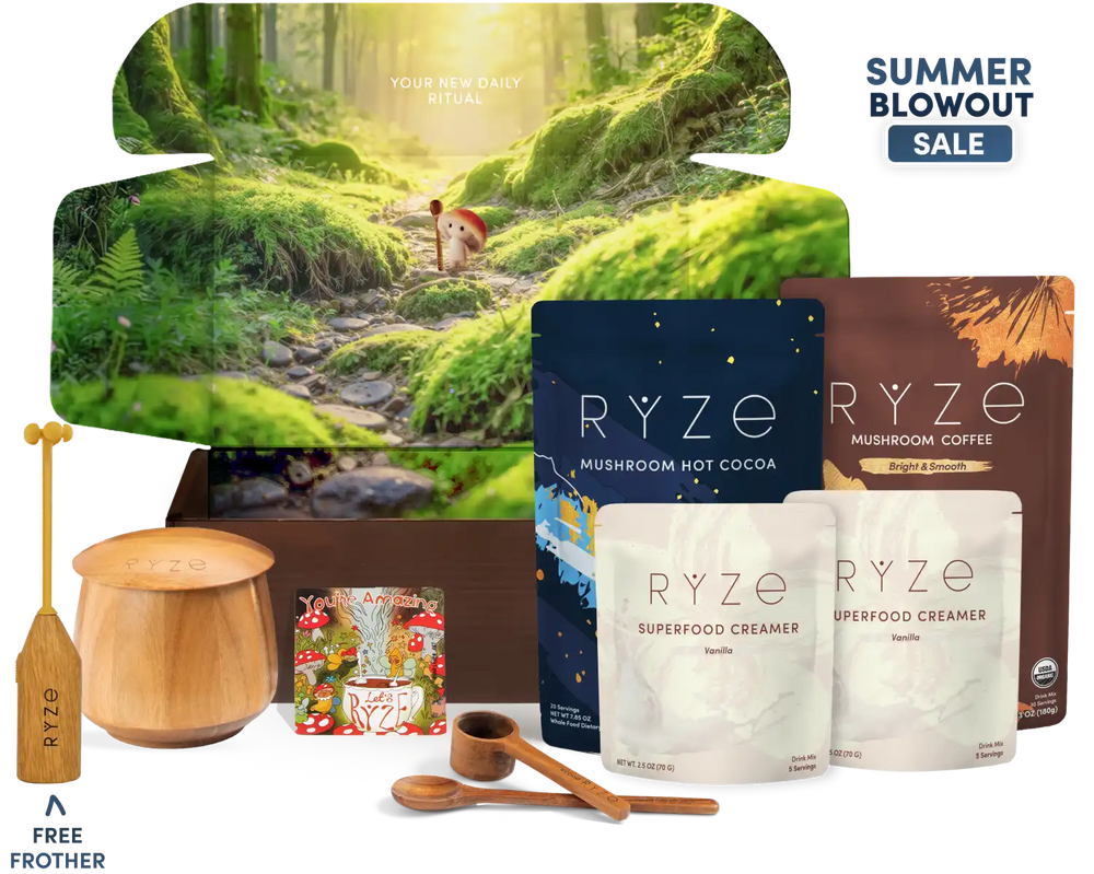 A curated wellness gift set arranged in front of a large illustrated forest box. Visible items include RYZE mushroom hot cocoa and mushroom coffee pouches, two white RYZE superfood creamer pouches, wooden spoons, a wooden cup, a wooden spoon, a small decorative magnet, and a tall wooden frother.