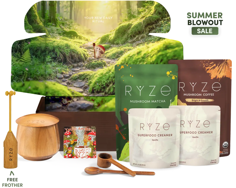 A curated wellness gift set arranged on a white background, featuring a large forest-themed box with a deer on a mossy path, several RYZE coffee and matcha pouches, two wooden spoons, a wooden cup, a wooden spoon, a small magnet, and a free frother offer graphic. Text in the top right reads 'SUMMER BLOWOUT SALE'.