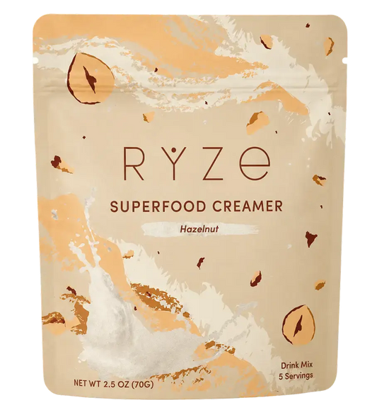 RYZE Superfood Creamer Hazelnut flavor in a 2.5 oz stand-up pouch, featuring a beige and peach design with illustrations of hazelnuts and a splash of cream.