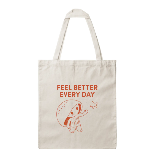 An off-white canvas tote bag with a red graphic of a cartoon mushroom and the text 'FEEL BETTER EVERY DAY' printed on the front, set against a plain white background.