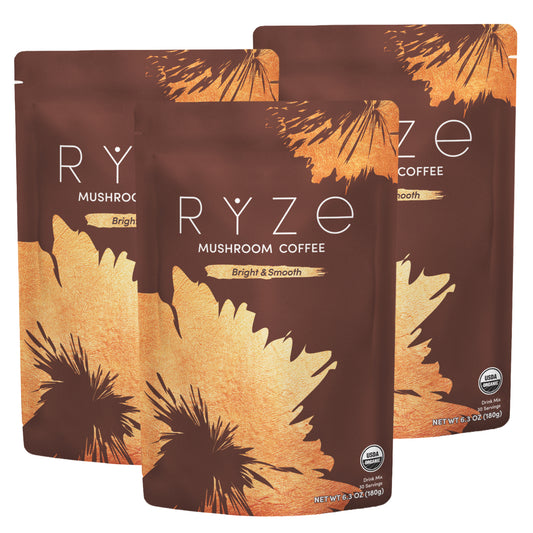 Three stand-up pouches of RYZE Mushroom Coffee arranged in a fan shape on a white background. The packaging is dark brown with a large gold leaf design and white text.