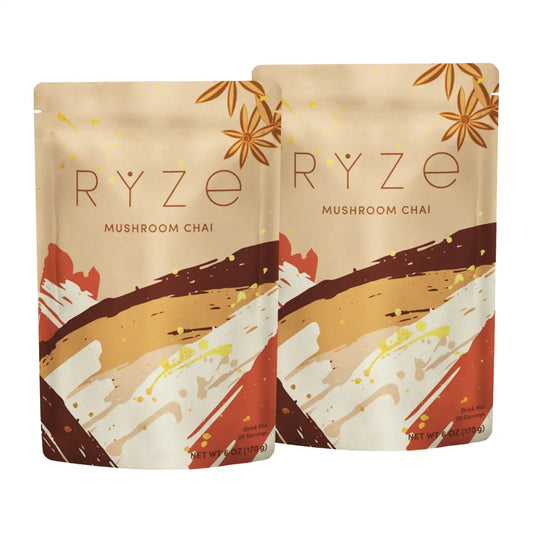 Two stand-up pouches of RYZE Mushroom Chai tea on a plain white background. The packaging features a warm beige background with brown star anise illustrations and abstract brushstroke patterns in brown, white, and red.