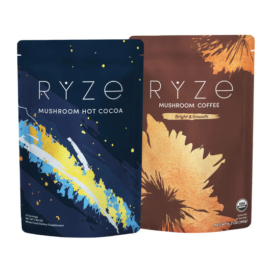 Two stand-up pouches of RYZE coffee and cocoa products on a light beige background. The left pouch is dark navy blue with yellow, white, and blue brushstroke artwork and reads 'RYZE MUSHROOM HOT COCOA.