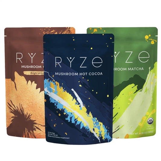 Three stand-up pouches of RYZE mushroom-based beverages are shown on a white background: Mushroom Hot Cocoa in blue, Mushroom Matcha in green, and the central Mushroom Coffee in brown. 