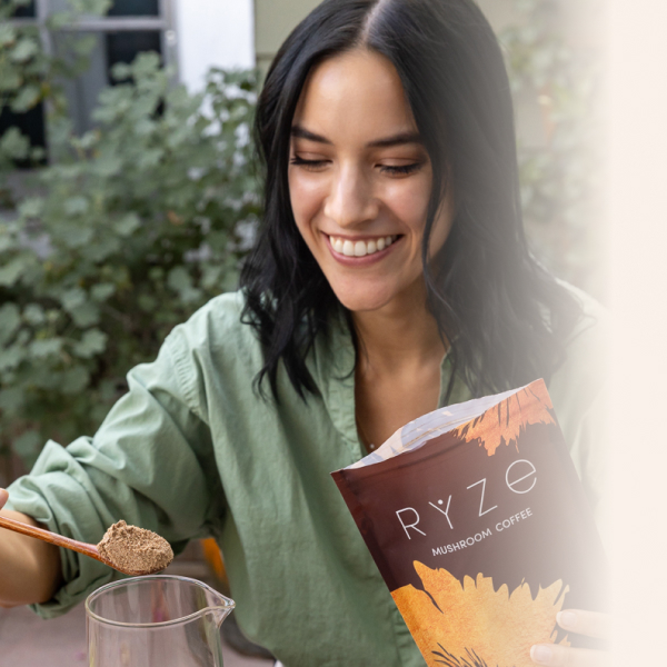 Person smiling while preparing Ryze mushroom coffee outdoors.
