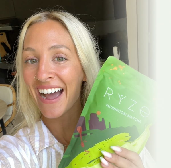 Person smiling and holding a green Ryze Mushroom Matcha package.