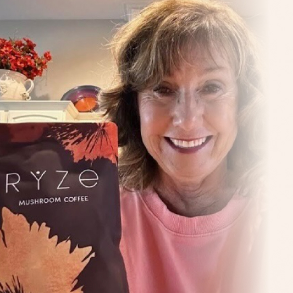 Smiling woman holding a package of Ryze mushroom coffee.