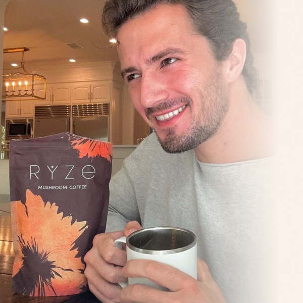 Person smiling with a mug, next to a bag of Ryze mushroom coffee.