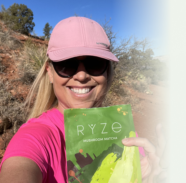 Person in pink shirt and cap holding Ryze Mushroom Matcha outdoors.