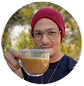 Person wearing a red beanie holding a cup of coffee outdoors.