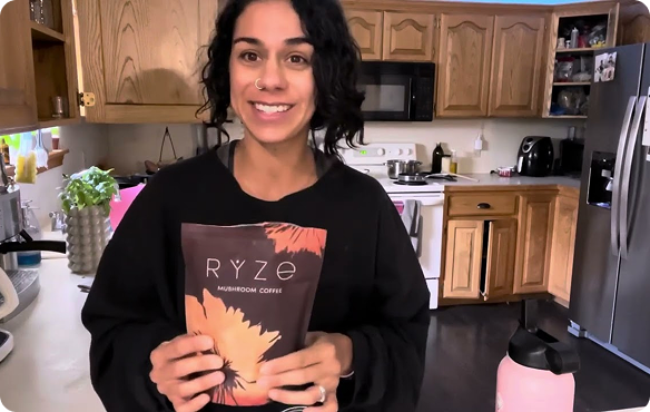 Person holding a package of Ryze mushroom coffee in a kitchen.